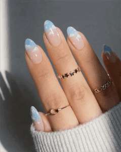 Soft blue ombre French tip nails with glossy finish and subtle star accents on natural almond-shaped nails