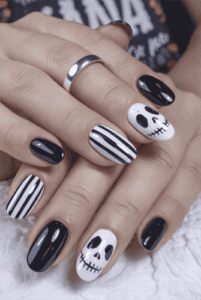 Black and white Halloween nails with skull art and striped design on glossy short almond nails, spooky nail art inspiration
