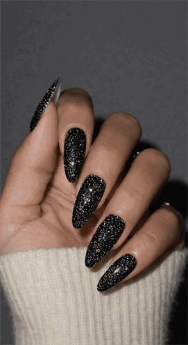 Long stiletto nails with black galaxy glitter polish, dense sparkling texture with multidimensional shimmer, bold night-sky inspired glam nail design