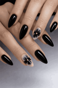 Almond-shaped glossy black nails with subtle floral accent design on nude base, minimalist 3D flower detail with high-shine elegant finish