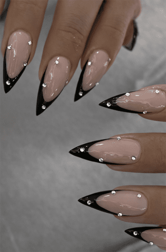 Long almond nails with nude base and black French tips, embellished with small rhinestones for subtle sparkle, elegant glam nail design