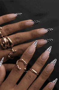 Long almond nails with nude base and black and white polka dot French tips, playful contrast design with glossy finish and trendy retro vibe