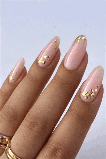 Medium almond nails with blush pink nude base and scattered gold metallic foil accents, glossy finish with soft romantic luxury nail design