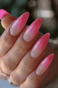 Long almond nails with pink glitter ombre fade from nude base, sparkling gradient effect with glossy finish and glamorous high-shine nail design