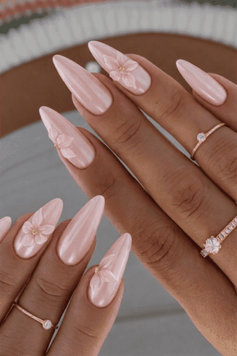 Long almond-shaped nails with soft pink pearlescent chrome finish and delicate 3D flower accents, glossy iridescent shine with elegant bridal-inspired floral nail design