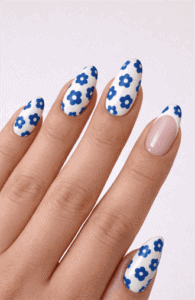 Almond-shaped nails with white base and blue daisy flower pattern, glossy finish with playful floral detail and fresh spring-inspired nail design