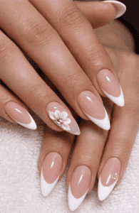Almond-shaped nails with nude base and classic white French tips, featuring 3D floral accent with rhinestone center, glossy elegant bridal nail design