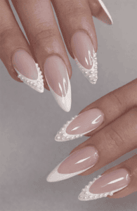 Almond-shaped nails with nude base and white pearl French tips, embellished with delicate bead detailing, glossy finish with refined bridal aesthetic