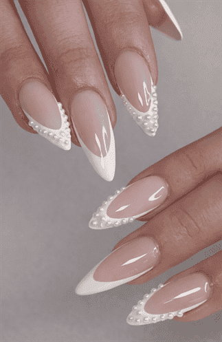 Almond-shaped nails with nude base and white pearl French tips, embellished with delicate bead detailing, glossy finish with refined bridal aesthetic