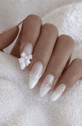 Almond-shaped nails with nude base and white French tips, featuring 3D bow and pearl accents, glossy finish with soft romantic bridal nail design