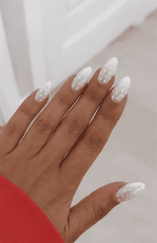 Almond-shaped nails with sheer white base and small white polka dot pattern, glossy finish with soft playful texture and minimalist nail design