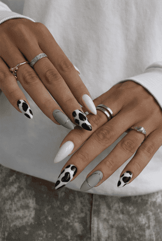 Sage green and cow print almond nails with glossy finish, black and white animal print accent nail design