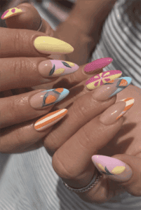 Colorful fruit nail art with pastel almond nails featuring lemons, oranges and striped designs on glossy nude base