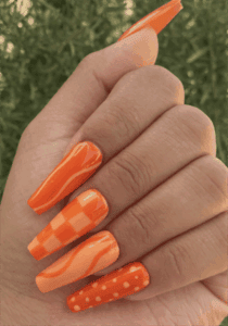 Bright orange mix and match coffin nails with checkerboard, swirl and polka dot nail art, glossy manicure