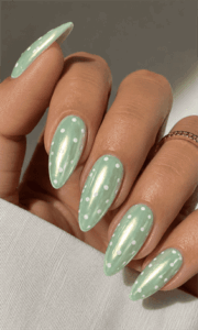 Mint pearl chrome almond nails with white polka dots, glossy pastel green nail design featuring iridescent shimmer finish