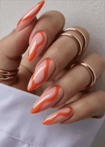 Orange swirl stiletto nails with nude base, glossy abstract wave nail design on long pointed nails