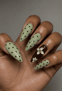 Sage green polka dot almond nails with brown accent nail and white floral nail art, glossy botanical manicure