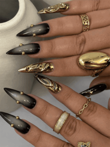 Smoky black ombre stiletto nails with gold chrome accents, luxury gothic nail design featuring metallic 3D details