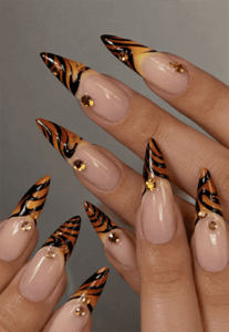 Tiger stripe French tip stiletto nails with nude base, orange and black animal print nail design featuring gold rhinestone accents