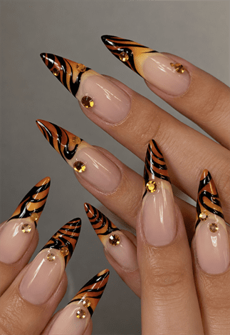 Tiger stripe French tip stiletto nails with nude base, orange and black animal print nail design featuring gold rhinestone accents