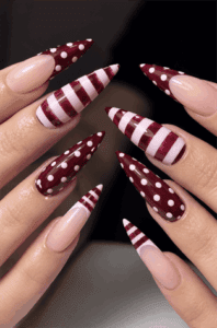Burgundy stiletto nails with glossy polka dot and candy stripe nail art, nude negative space accents and elegant retro manicure design