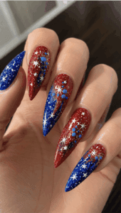 Glitter patriotic ombré stiletto nails featuring red and blue sparkle fade, white fireworks, stars and rhinestone accents for a bold Fourth of July manicure