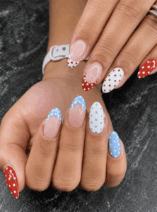 Patriotic mix and match almond nails featuring red, white and blue polka dots, scalloped French tips and glossy Fourth of July nail art