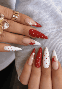 Red and white star stiletto nails with polka dot accents, glossy patriotic nail design on a nude base featuring bold Americana-inspired nail art