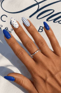 Royal blue almond nails with minimalist accent nail art featuring blue stripes and white polka dots, glossy modern manicure design