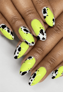 Neon yellow cow print almond nails with black and white animal print accents, glossy western-inspired manicure and bold statement nail design