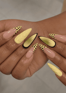 Butter yellow almond nails with black polka dot French tips, abstract aura accents and 3D textured nail art on a glossy nude base