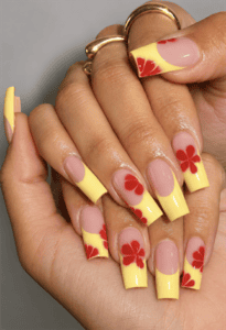 Pastel yellow French tip coffin nails with red hibiscus flower nail art, glossy nude base and tropical summer manicure design