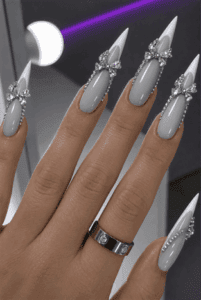 Elegant silver bow French stiletto nails with glossy milky white polish, crystal rhinestone bows and luxury bridal nail design