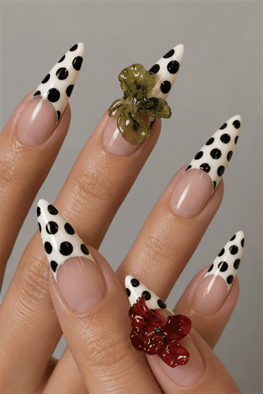 Black polka dot French tip stiletto nails with 3D floral embellishments, glossy nude base and retro-inspired statement nail design
