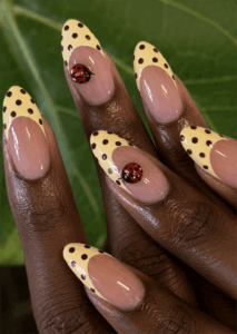 Ladybug French tip almond nails with pastel yellow polka dot tips, 3D ladybug accents and glossy nude base