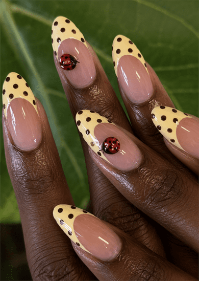 Ladybug French tip almond nails with pastel yellow polka dot tips, 3D ladybug accents and glossy nude base