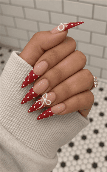 Red polka dot French tip stiletto nails with white 3D bow accents, glossy nude base and festive coquette-inspired nail design
