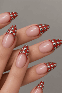 Red studded French tip stiletto nails with silver metallic studs, glossy nude base and edgy luxury nail design