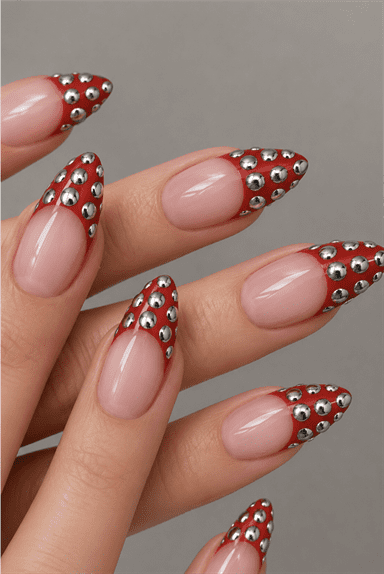Red studded French tip stiletto nails with silver metallic studs, glossy nude base and edgy luxury nail design