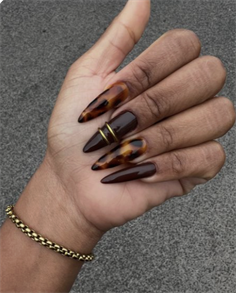 Long stiletto nails with glossy chocolate brown polish, tortoise shell accents, and delicate gold detailing