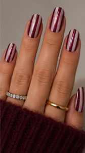 Short square nails with alternating burgundy and shimmering white vertical stripes and glossy finish.