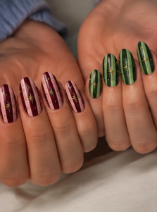 Short oval burgundy and forest green nails with vertical stripes, delicate gold starbursts and glossy finish.