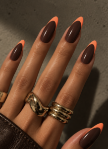 Long almond nails painted glossy chocolate brown with vibrant orange French tips and curved edges.