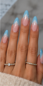 Long almond nails with sheer pink bases fading into silver glitter and icy blue tips.