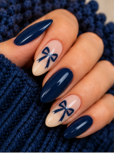 Long almond nails with glossy navy blue polish, nude bow accents and tiny silver embellishments.